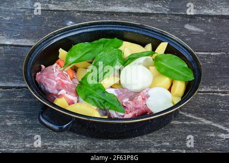 Raw lamb steaks in a pot, seasoned and  arranged with different sorts of cultivated and wild vegetables, onion, potato, carrot and ramson, ready to be Stock Photo