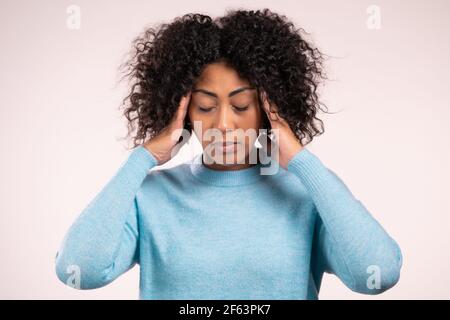 Portrait of african woman having headache, white studio portrait. Girl putting hands on head. Concept of migraine problems, medicine, illness Stock Photo