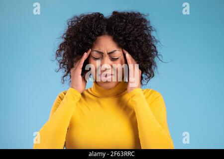 Portrait of african woman having headache, blue studio portrait. Girl putting hands on had. Concept of migraine problems, medicine, illness Stock Photo