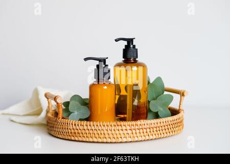 Amber glass liquid soap dispenser bottles and eucalyptus in rattan tray on table in bathroom. SPA organic natural cosmetic products set. Stock Photo