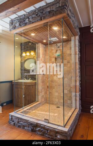 Beige and tan ceramic and cut stone shower stall with three-sided clear glass panels, cedar wood ceiling and vanity in open design bathroom Stock Photo