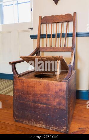 Opened antique wooden armchair toilet in living room inside an old 1825 Canadiana cottage style fieldstone home Stock Photo