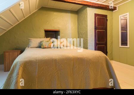Pine wood-frame double bed with cream coloured bedspread and old wooden closet door in guest bedroom with white painted wide pine wood floorboards Stock Photo