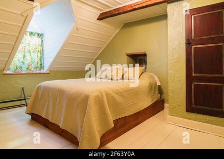 Pine wood-frame double bed with cream coloured bedspread and old wooden closet door in guest bedroom with white painted wide pine wood floorboards Stock Photo