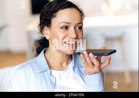 Attractive successful mixed race brunette attractive woman, using smartphone, talking to friends or colleagues on speakerphone or recording audio message, looking away, smiling friendly Stock Photo