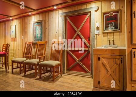 High back wooden chairs along a wood plank wall and vanity with galvanized bucket sink and rustic brass coloured faucets in basement game room Stock Photo
