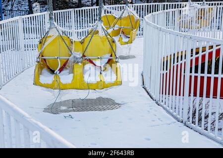 Swinging ride yellow seats covered with snow. Winter amusement park ...