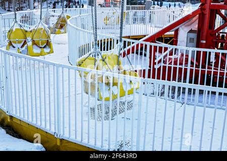 Swinging ride yellow seats covered with snow. Winter amusement park ...