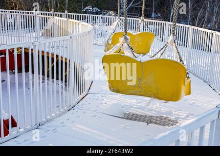 Swinging ride yellow seats covered with snow. Winter amusement park ...