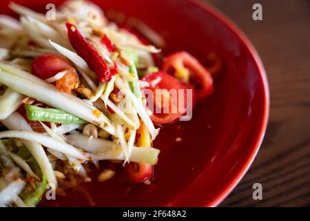 som tam thai, green papaya salad and spicy in red plate on wooden background, Thai food or Northeastern food Stock Photo