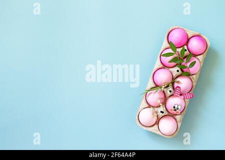 Minimal Easter concept. Festive spring mood, natural decor. Easter eggs in pink tones and gerbera flower on pastel blue background. Top view flat lay. Stock Photo
