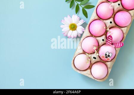 Minimal Easter concept. Festive spring mood, natural decor. Easter eggs in pink tones and gerbera flower on pastel blue background. Top view flat lay. Stock Photo