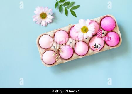 Minimal Easter concept. Festive spring mood, paper box with Easter eggs in pink tones and gerbera flower on pastel blue background. Top view flat lay. Stock Photo