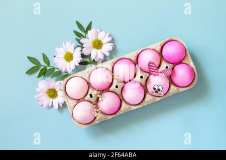 Minimal Easter concept. Festive spring mood, paper box with Easter eggs in pink tones and gerbera flower on pastel blue background. Top view flat lay. Stock Photo