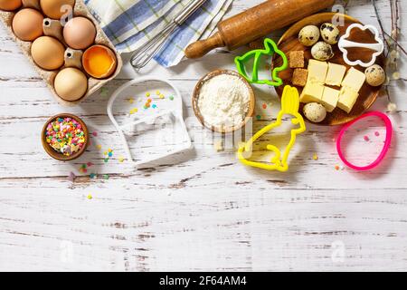 Baking background. Ingredients for Easter festive baking - flour, brown sugar, eggs, butter, confetti on rustic kitchen table. Flat lay. Top view. Cop Stock Photo