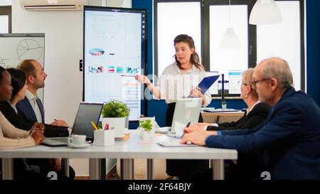 Female executive leader coach presenter giving financial presentation in modern office boardroom for corporate employees group, speaker mentor explaining training professional team at business seminar Stock Photo