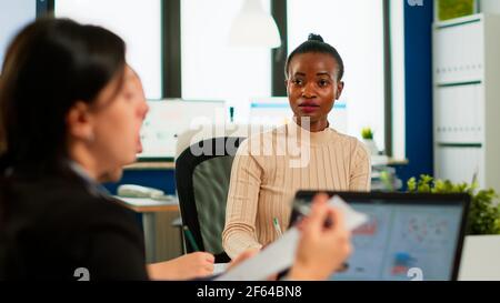 Confident african leader negotiating with business group explaining contract benefits at formal board meeting consulting corporate clients presenting commercial offer sitting at conference office table Stock Photo