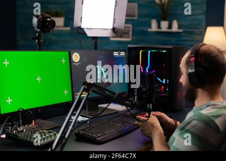 Professional cyber streamer playing digital videogames on professional powerful computer with green screen display. Player using pc with mock up chroma isolated desktop streaming shooter games Stock Photo