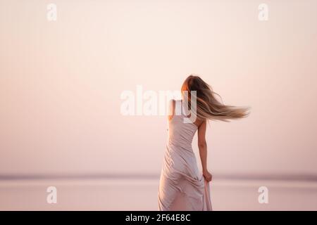 Portrait of a young blonde woman in an evening airy pastel pink, powdery dress against a background of beautiful sunset. Girl with natural make-up, ha