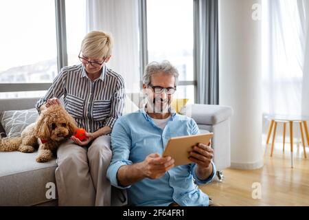 Beautiful happy mature couple is using a digital tablet, talking and smiling at home Stock Photo