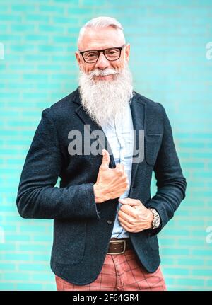 Vertical portrait of hipster man with elegant outfit posing against turquoise wall background - Trendy old people wearing casual fashion cloth Stock Photo