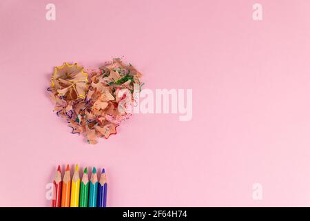 sharpened colored pencils and heart-shaped pencil shavings on pastel pink color. Rainbow or LGBT pencils. Decoration for St. Valentine's Day. Top view