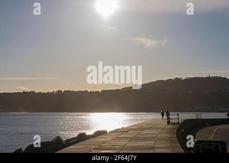 Landscape panorama view of coastal seaside harbor front quayside with couple walking in silhouette at dusk sunset Stock Photo