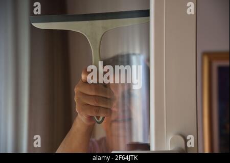 Senior woman using a squeegee to wash a window Stock Photo