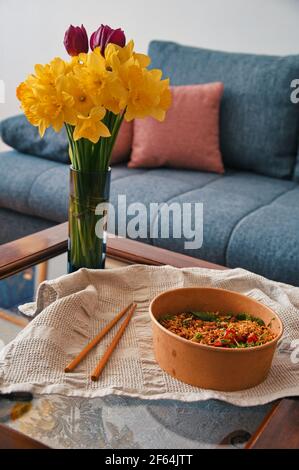 Takeout Asian food with chopsticks on table decorated with flowers in vase Stock Photo