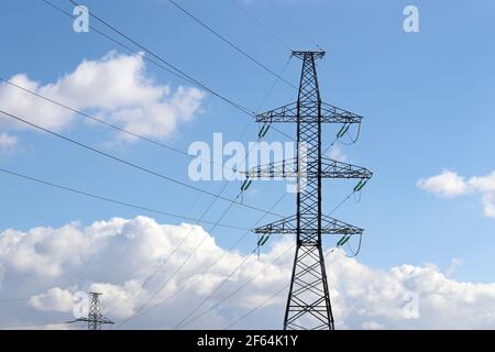 High voltage towers with electrical wires on blue sky with white clouds. Electricity transmission lines, power supply concept Stock Photo