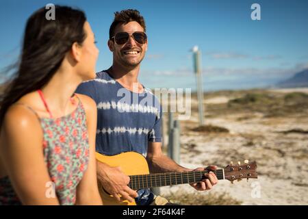 Happy caucasian couple on beach by the sea playing guitar Stock Photo