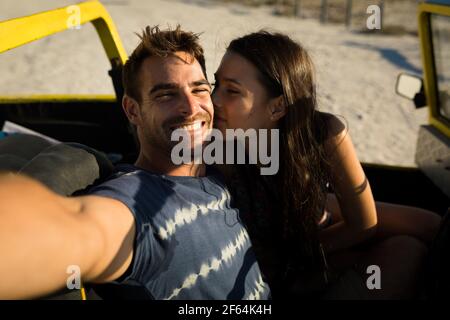 Happy caucasian couple sitting in beach buggy by the sea taking selfie Stock Photo