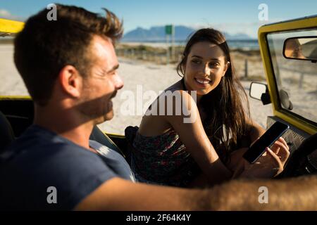 Happy caucasian couple sitting in beach buggy by the sea using smartphone Stock Photo
