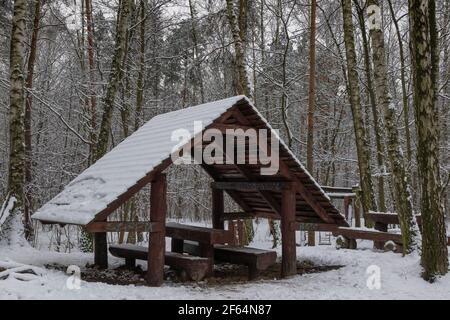 Rest area in winter forest for tourists, travellers, wooden shelter with bench, table and snow covered roof Stock Photo