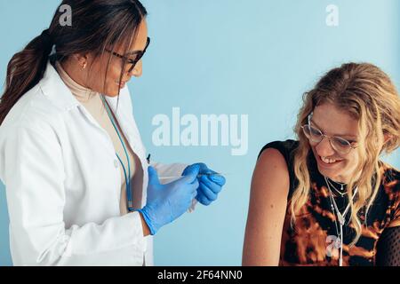 Smiling young woman getting vaccine from a female doctor. Healthcare professional vaccinating a woman. Stock Photo