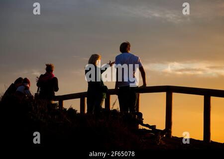 Young couple standing on balustrade on cliff line in front of the ocean and watching the sunset Stock Photo