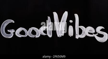 Text on glass 'Good Vibes' made with white paint. Inspirational message text to motivate to positive expressions. Black background. High quality photo Stock Photo