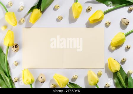Colorful easter quail eggs and tulips on white background with brochure. Flat lay. Happy easter greeting card. Stock Photo