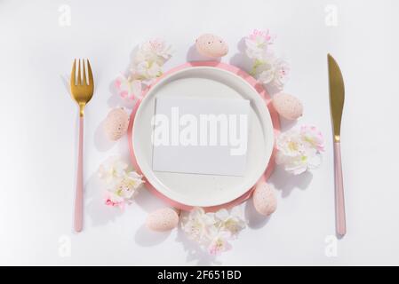Easter table place setting with eggs, plate, cutlery and beautiful flowers, top view composing with card Stock Photo
