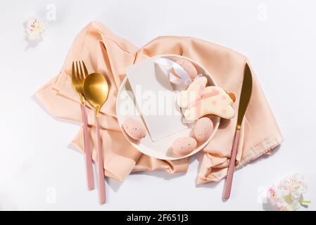 Easter table place setting with eggs, bunny cookies, plate, cutlery and beautiful flowers with menu Stock Photo