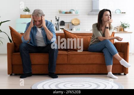 Portrait of mid-adult couple sitting on sofa after quarrel. Stock Photo