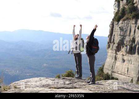 Two excited hikkers celebrating vacation raising arms in the mountain