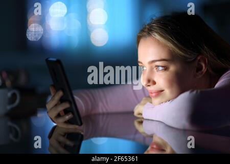 Satisfied teen watching smart phone content on a table in the night at home Stock Photo