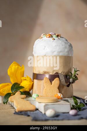 Easter composition with traditional Orthodox sweet bread. Kulich decorated with meringue icing, candy shaped eggs, easter cookies and tulip. Selective Stock Photo
