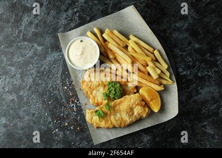 Baking paper with fried fish and chips on black smokey table Stock Photo