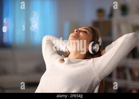 Relaxed woman listening to music wearing headphones sitting on a chair in the night at home Stock Photo