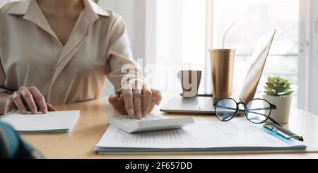 Close up hand of woman using computer calculating household finances or taxes on machine, female manage home family expenditures, using calculator Stock Photo