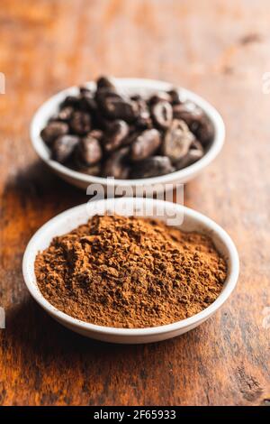 Roasted cocoa beans and cocoa powder in bowl on wooden table. Stock Photo