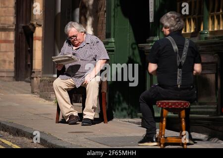 A man reads a newspaper in the sun in Central Lodnon. Picture date: Tuesday March 30, 2021. Temperatures in parts of the UK are expected to be significantly warmer this week as families and friends are reunited and sporting activities are allowed to resume in England. Stock Photo