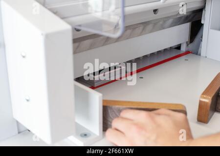 a specialist operator works on an automatic paper cutting machine, a professional cutter, equipment for a printing house or workshop Stock Photo